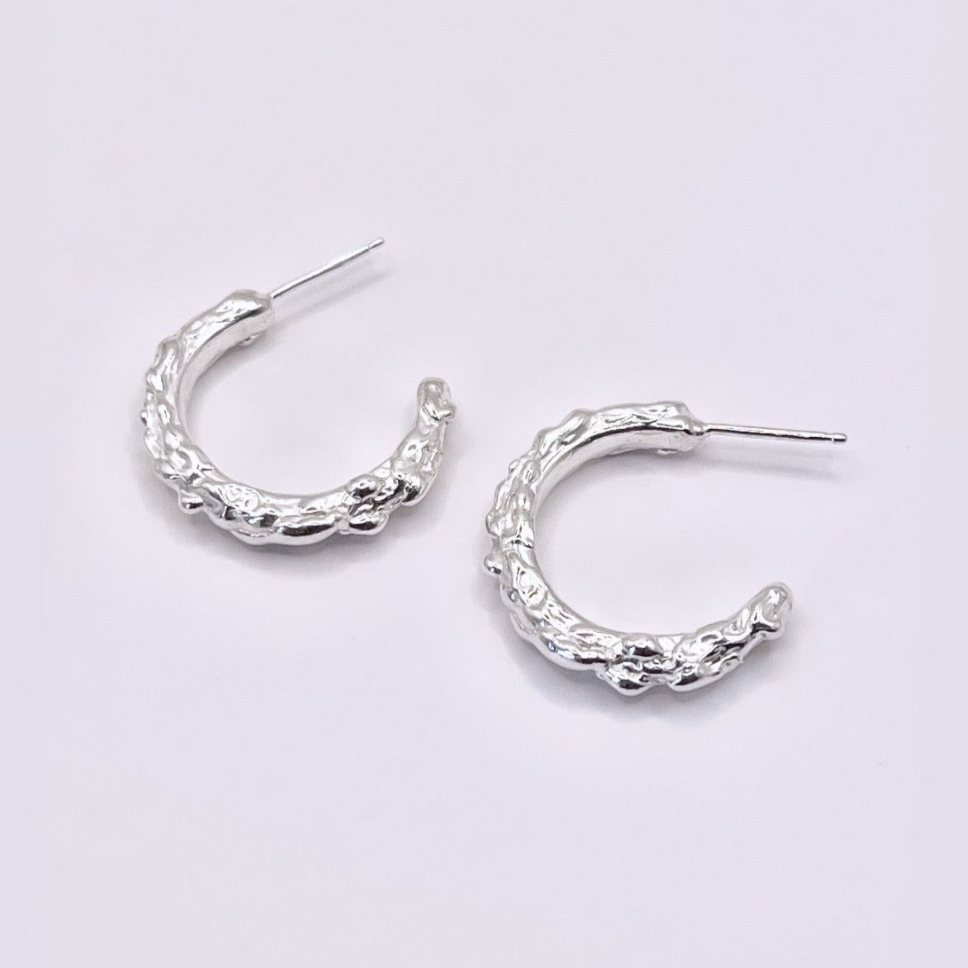 Silver hoop earrings with molten organic texture on a grey background