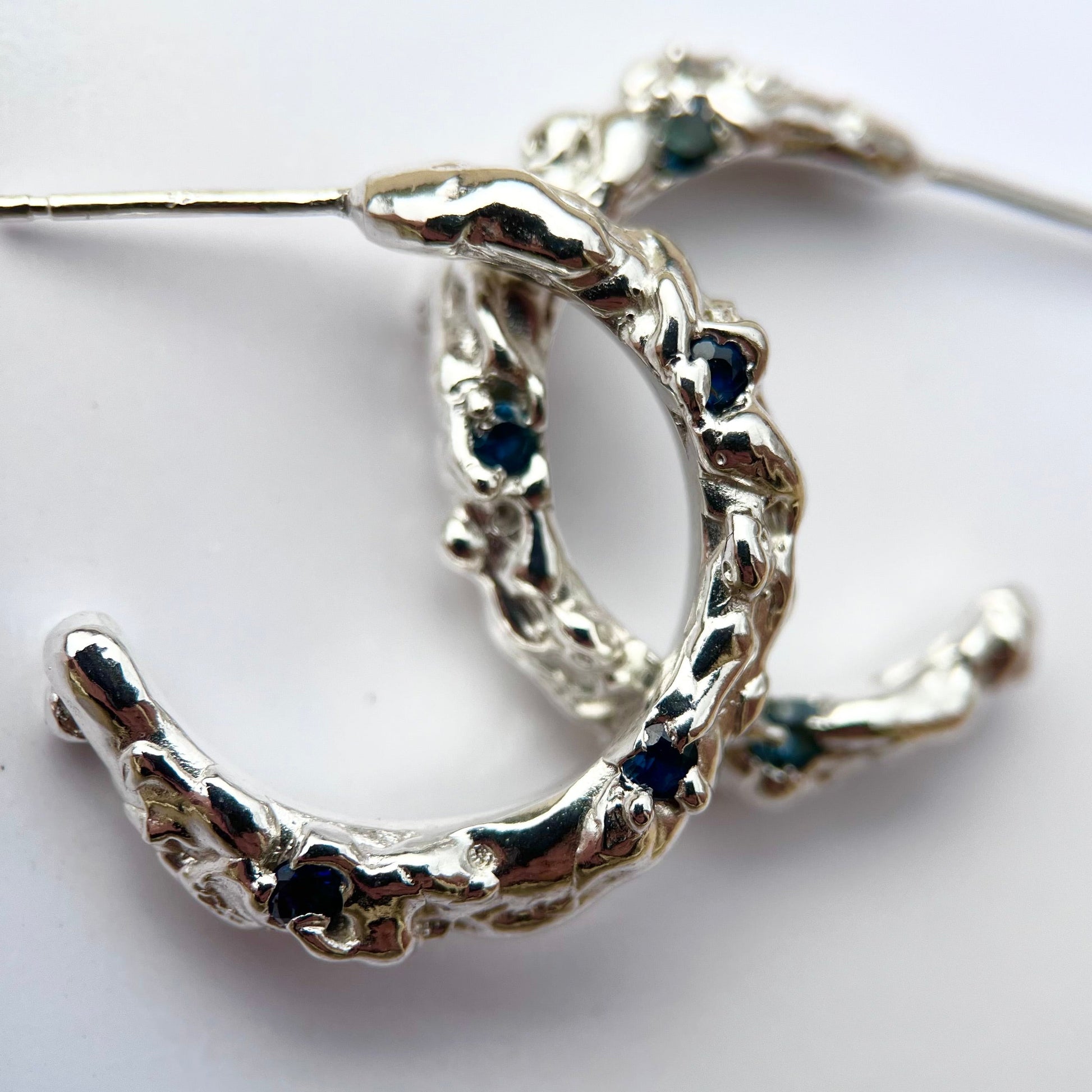 Silver hoop earrings with molten organic texture featuring three blue/green sapphires on each hoop