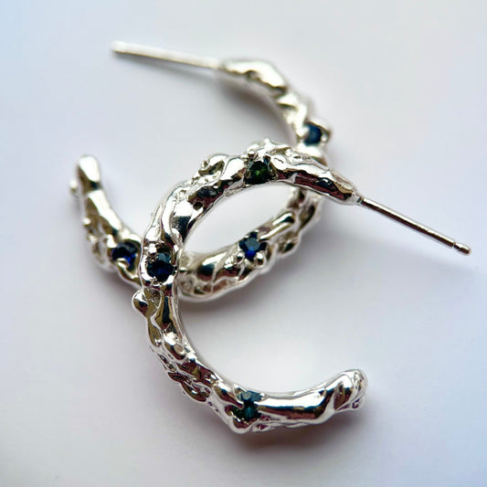 Silver hoop earrings with molten organic texture featuring three blue/green sapphires on each hoop