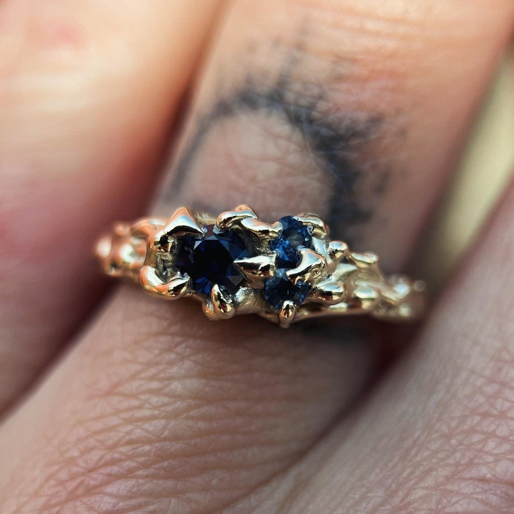 Ethereal gold ring with three deep blue sapphires and a vine like texture on the ring face