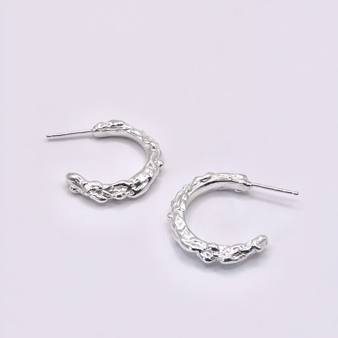 Silver hoop earrings with molten organic texture on a grey background