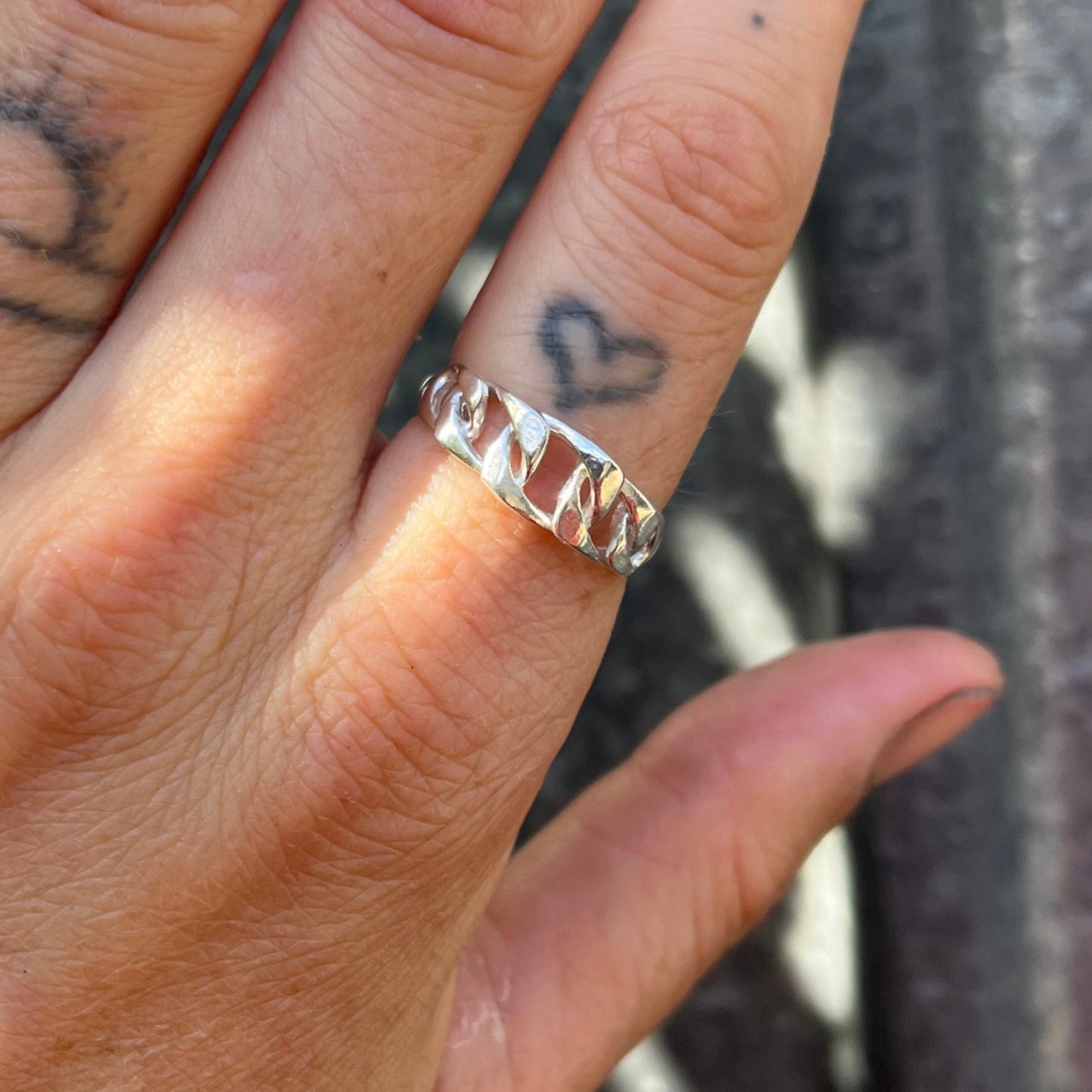 Chain ring with organic texture worn on hand with tattoos with a grey background