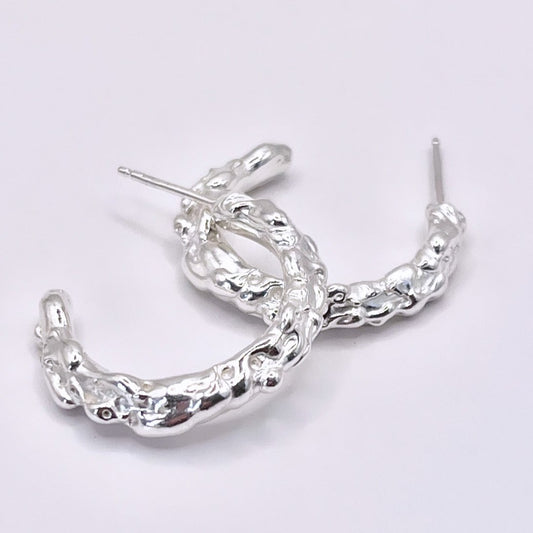 Silver hoop earrings with molten organic texture on a grey background