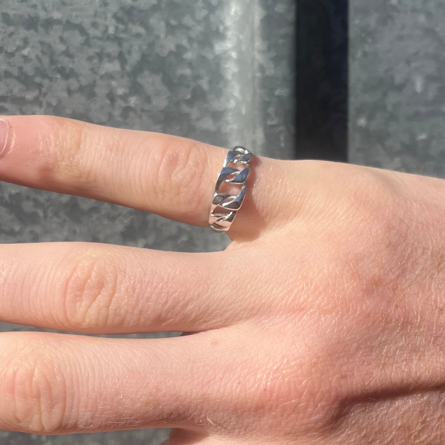 Chain ring with organic texture worn on hand with tattoos with a grey background