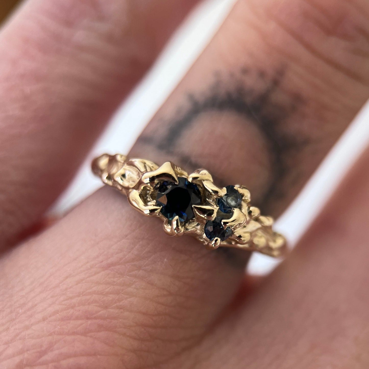 Ethereal gold ring with three deep blue sapphires and a vine like texture on the ring face